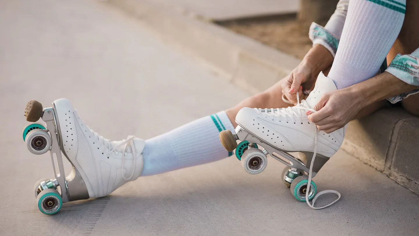 Une personne lace ses patins à quatre roues blancs, photographiés en gros plan.